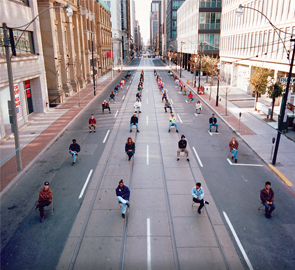 Second image of four, the cars are removed, but the drivers remain in their seats on the street, still taking up a large amount of road space.